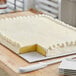 A white full sheet cake on a white double-wall corrugated cake board with a slice missing.