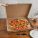 A hand holding a 24" white corrugated pizza circle in a box on a table.