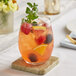 A close up of an Acopa stemless wine glass filled with a fruity drink garnished with berries and mint.
