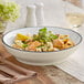 A bowl of pasta with vegetables and herbs in an Acopa Embers cream white stoneware bowl.
