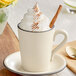 A Acopa cream stoneware mug filled with coffee topped with whipped cream and a cinnamon stick.