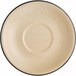 A close-up of an Acopa Harvest Tan matte stoneware saucer with black speckles.