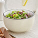 A cream white stoneware bowl filled with salad on a table.