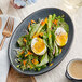 An Acopa Midnight Blue Matte coupe stoneware platter with a salad of greens, eggs, and vegetables.
