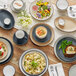A cream white matte stoneware cup with a handle, shown as part of a table setting with various dishes.