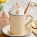 A cup of coffee with whipped cream and a cinnamon stick in an Acopa Harvest Tan stoneware mug.