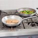 A Vollrath Wear-Ever fry pan with chicken and vegetables cooking on a stove.