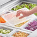 A hand using a Vigor translucent polypropylene lid to cover a plastic food container of salad.