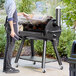 A man cooking meat on a Backyard Pro wood-fire pellet grill.