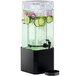 A Cal-Mil square acrylic beverage dispenser with a black metal base, ice, and cucumber slices.