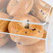 A Cal-Mil clear acrylic food bin filled with blueberry bagels on a bakery display counter.