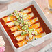 A dish of enchiladas with avocado and cheese smothered in sauce on a white dish.