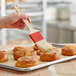 A person using a Thermohauser natural bristle pastry brush to spread pastry on a tray of pastries.