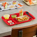 A red Choice heavy-duty melamine tray with 7 compartments holding food on a table.