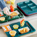 A Choice ocean teal compartment tray with food and a fork on a blue surface.