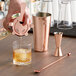 A person using an Acopa copper cocktail shaker to pour a drink.