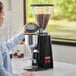 A woman using an Estella Caffe On Demand Espresso Grinder in a professional kitchen.