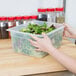 A person holding a Cambro translucent polypropylene food pan of salad greens.