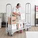 A man in a white hat and apron loading boxes onto a Lavex aluminum folding utility cart.