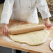 A person using a Choice 18" Wood Rolling Pin to roll out dough on a wooden board.