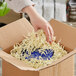 A hand putting Spring-Fill Ivory Crinkle Cut paper shred into a cardboard box.