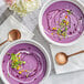 Two bowls of purple sweet potato soup with white cream and green sprouts, flowers, and spoons.