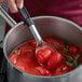 A hand stirring Furmano's whole peeled tomatoes in a pot on the stove.