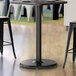 A Lancaster Table & Seating black metal round column table base supporting a table with two stools.