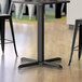 A black Lancaster Table & Seating counter height table base with a black pole and black base.