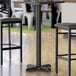 A black Lancaster Table & Seating bar table base with two chairs at a table.