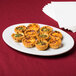 A Tuxton Alaska white china oval platter with mini quiches topped with cheese and bacon.