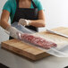 A person in a black apron cutting meat on a table with a knife and placing it in an ARY VacMaster plastic bag.