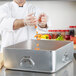 A chef pouring carrots into a large silver Vollrath aluminum double roaster pan.