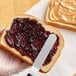 A person spreads Polaner Grape Jelly on a piece of bread.
