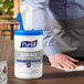 A person's hand holding a white plastic container of Purell Professional Surface Disinfecting Wipes.