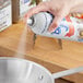 A person spraying Baker's Joy release spray onto a silver pan.