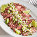 A plate of grilled TenderBison flank steak with lime wedges.
