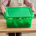 A woman wearing a white apron placing a green Vigor bus tub lid on a container of food.