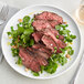 A plate with a TenderBison hanging tender steak, peas, and greens on a table with a knife and fork.