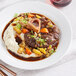 A white plate with a center-cut bison osso bucco and vegetables on a table.
