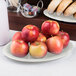 A Carlisle bone oval melamine platter with a plate of apples on a table.