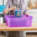 A woman using a purple Vigor bus tub to hold a box of pasta.