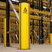 A yellow and black A-Safe RackGuard on a yellow pole in a warehouse.