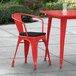A red metal chair with a black cushion on a patio.
