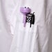 A white Chef Revival chef coat with black piping and a purple pen in the pocket.
