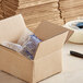 A close-up of a Lavex Kraft corrugated shipping box with a pen and a box of packaging inside.