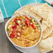 A bowl of Grecian Delight roasted red pepper hummus with vegetables and pita bread.