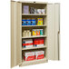 A tan Hallowell storage cabinet with solid doors and various items inside.