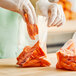 A gloved hand putting carrots in a Choice plastic bag.