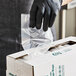 A person in black gloves putting a plastic bag into a white box.